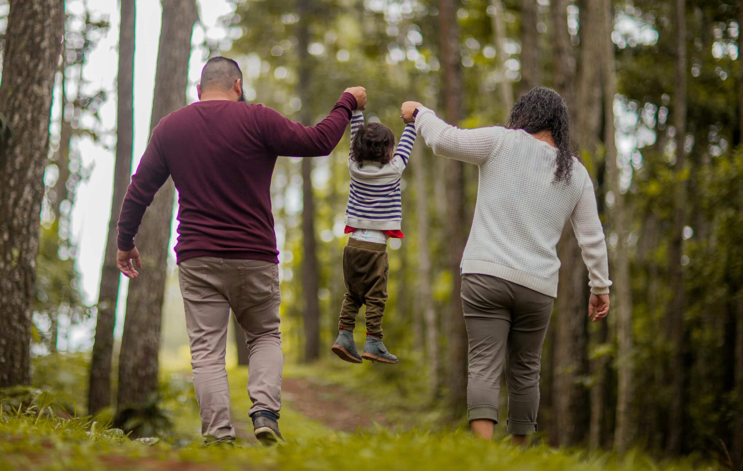 2. A family strolls through a vibrant forest, holding hands and enjoying nature together amidst the greenery.