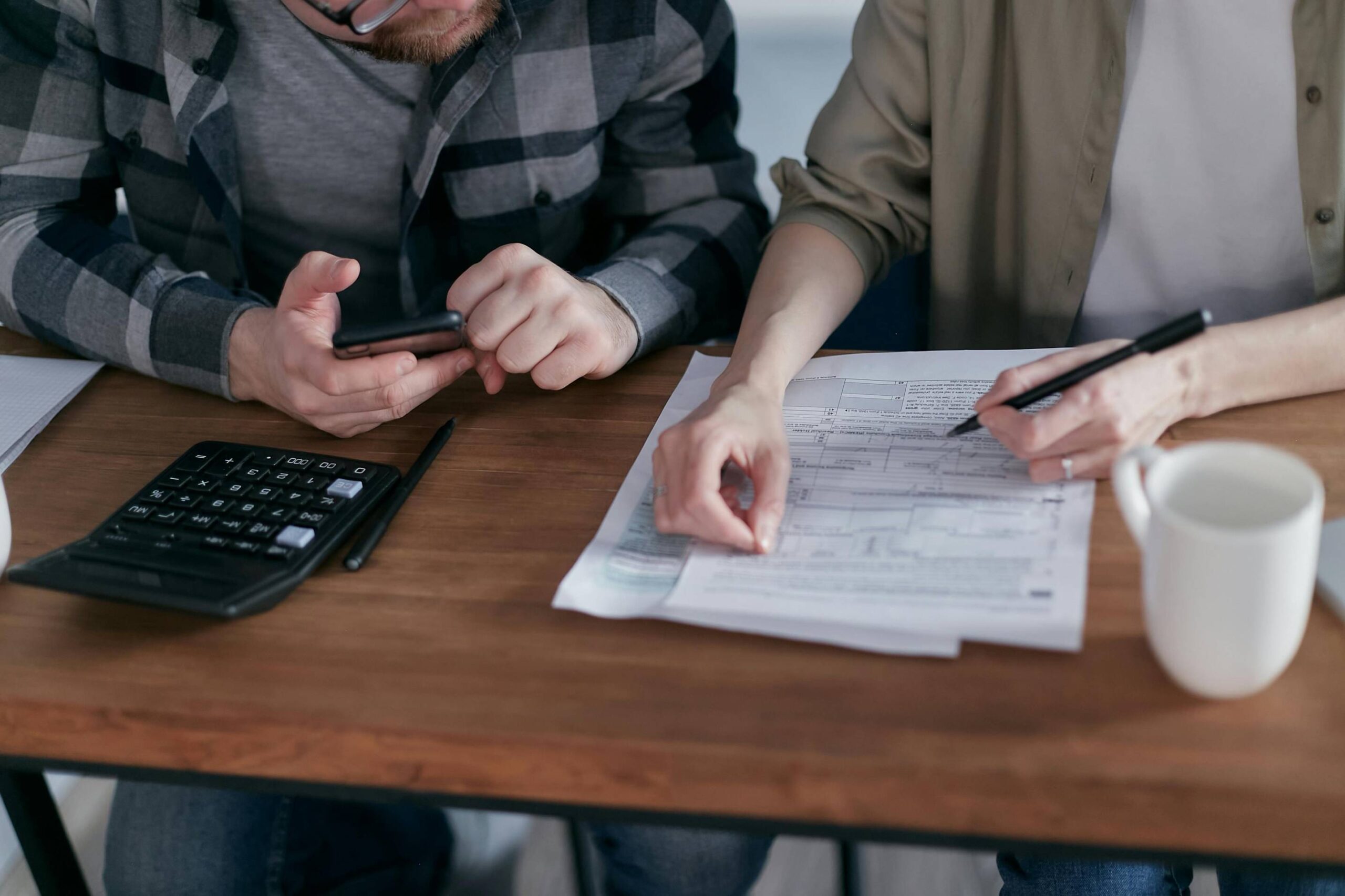 A table with two individuals discussing documents and using a calculator for tax analysis.
